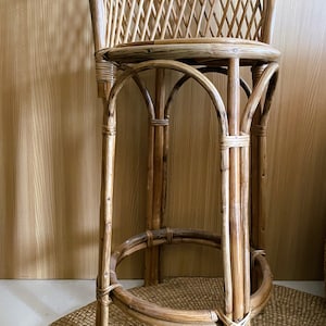 May include: A brown rattan bar stool with a woven back and a round seat. The stool has a curved base with four legs.