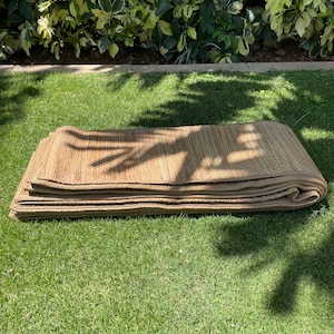 May include: A folded brown woven mat made of natural materials, lying on a green grassy lawn.
