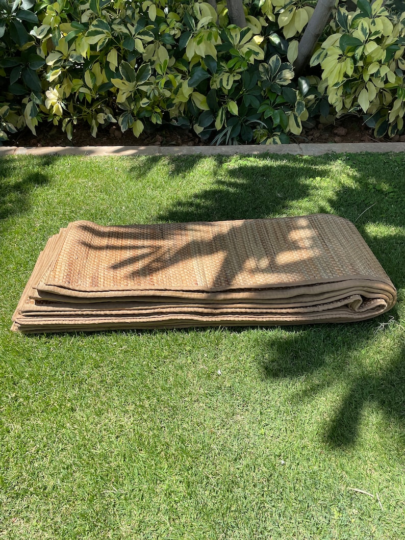 May include: A folded brown woven mat made of natural materials, lying on a green grassy lawn.