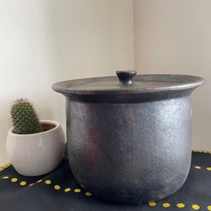 Puede incluir: Una olla de cerámica negra con tapa y pomo de madera. La olla está sobre una tela negra con lunares amarillos.