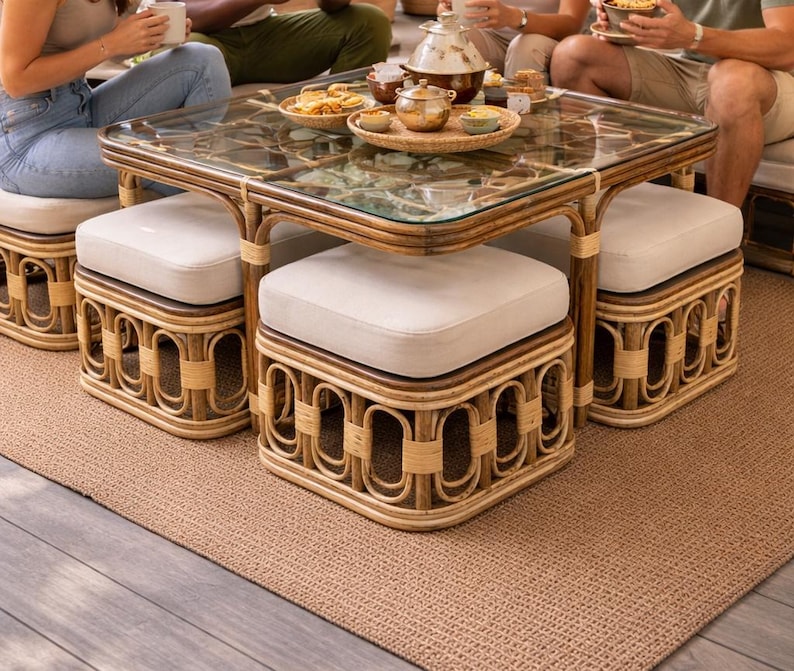 May include: A square coffee table with a glass top and a brown rattan frame, featuring four matching square ottomans with off-white upholstered cushions that tuck neatly underneath the table frame when not in use.