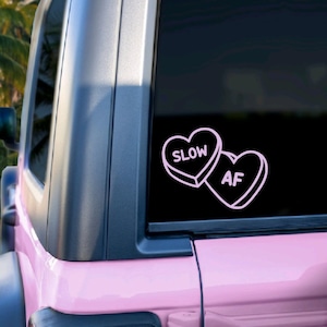 May include: A pink Jeep with a black window sticker that says "SLOW AF" in the shape of two pink candy hearts.