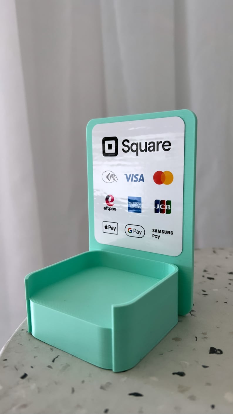 May include: A teal blue Square stand with a white sign that says "Square" and displays logos for various payment methods including Visa, Mastercard, American Express, Discover, JCB, Apple Pay, Google Pay, and Samsung Pay.
