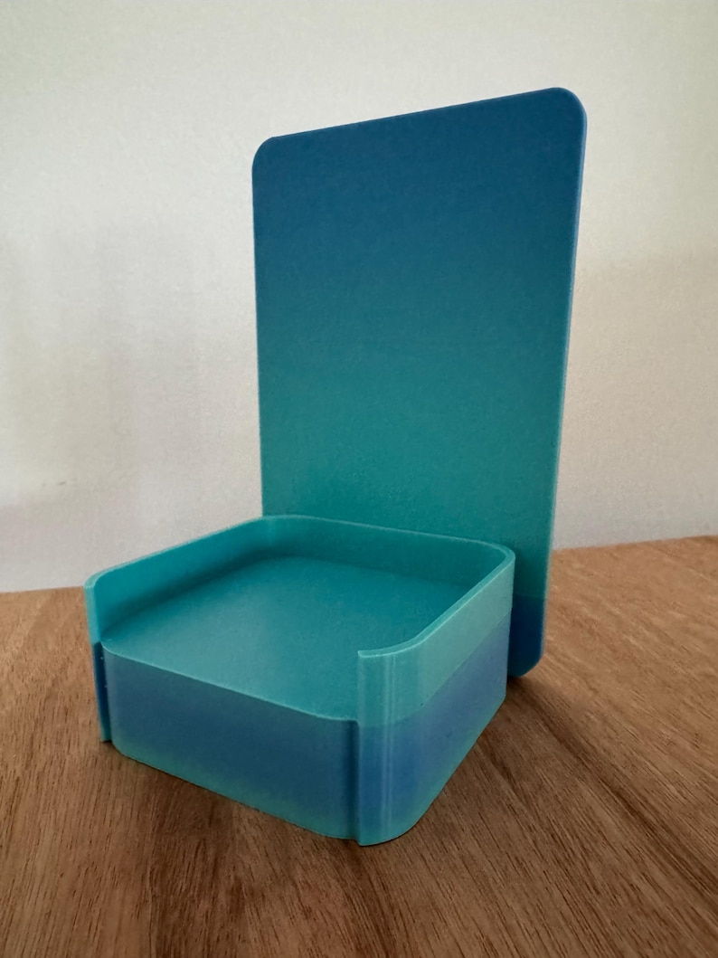 May include: A teal blue 3D printed phone stand with a square base and a tall rectangular back.