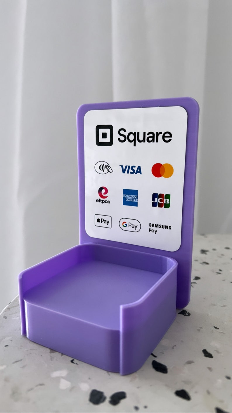 May include: A purple Square stand with a white sign that says "Square" and displays logos for Visa, Mastercard, American Express, Discover, JCB, Apple Pay, Google Pay, and Samsung Pay.