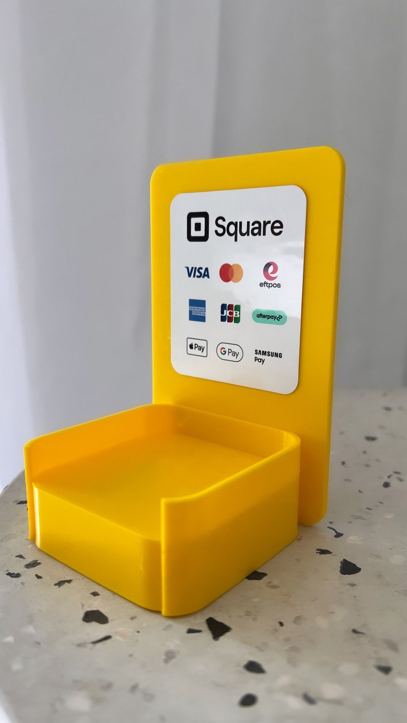 May include: A yellow plastic stand with a Square logo and a list of accepted payment methods including Visa, Mastercard, American Express, Discover, JCB, Afterpay, Apple Pay, Google Pay, and Samsung Pay.