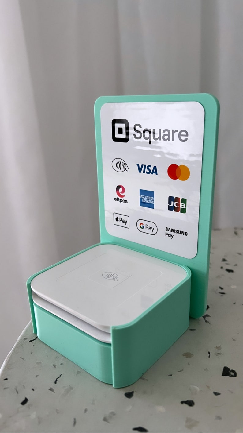 May include: A mint green Square payment terminal with a white card reader and a stand displaying logos for Visa, Mastercard, American Express, Discover, JCB, Apple Pay, Google Pay, and Samsung Pay.