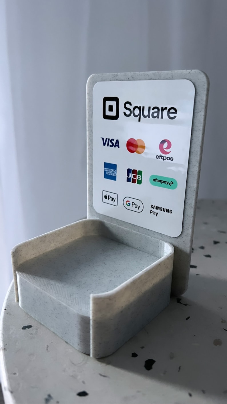 May include: A white plastic stand with a Square logo and a list of accepted payment methods including Visa, Mastercard, American Express, JCB, Discover, Apple Pay, Google Pay, Samsung Pay, Afterpay, and eftpos.