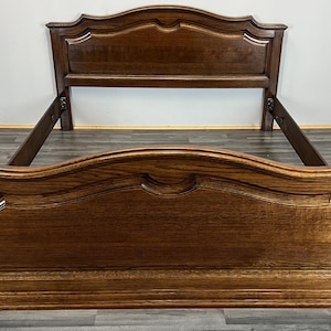 May include: A dark brown wooden bed frame with an ornate headboard and footboard. The frame has a curved design with decorative detailing. The bed frame is made of wood and has a glossy finish. The bed frame is designed for a standard size mattress.