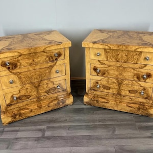 May include: A pair of wooden bedside cabinets, each with three drawers. The cabinets feature a light brown burl wood grain and silver knobs. The tops are rectangular. Each cabinet is approximately 60 cm wide.