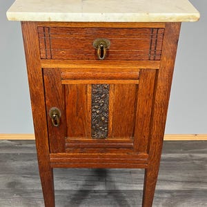 May include: A vintage wooden bedside table with a marble top, a single drawer, and a cabinet door with a decorative metal panel. The bedside table has turned legs and brass hardware.