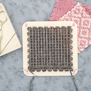 May include: A close-up of a grey woven fabric on a white loom with the word "Patches" printed on it. The loom has numbers 1 through 4 printed on it.