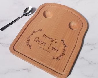 May include: A wooden serving tray shaped like a slice of toast with two indentations for eggs. The tray is engraved with the text "Daddy's Dippy Eggs" and "Love Oscar xxx" in a cursive font.
