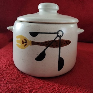 May include: White ceramic crock with a lid, featuring a brown, yellow, and black design of a fork, spoon, and ladle.