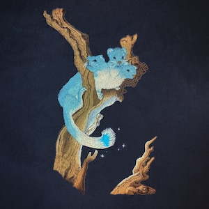May include: Embroidered artwork featuring three blue and white creatures perched on a brown tree branch against a dark blue background. The creatures have long tails with blue tips. The artwork includes small, sparkling stars.