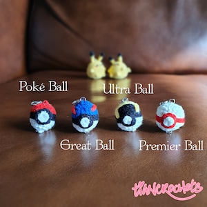 May include: Five crocheted Poké Balls in different colours and designs. The Poké Balls are labelled "Poké Ball", "Ultra Ball", "Great Ball", and "Premier Ball".