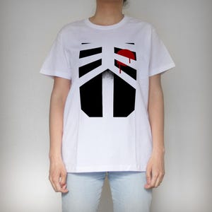 Puede incluir: Camiseta blanca con un gráfico en blanco y negro de una caja torácica con un corazón rojo y sangre goteando.