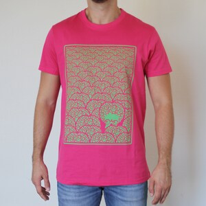 Könnte beinhalten: Ein pinkfarbenes T-Shirt mit einem grün-pinken Grafikdruck eines sich wiederholenden Musters aus Wirbeln und einem Gesicht mit Brille in der Mitte.