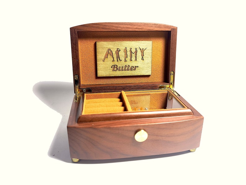 Puede incluir: Una caja de m&uacute;sica de madera con una tapa con bisagras y un pomo de lat&oacute;n. La tapa est&aacute; abierta y revela un peque&ntilde;o compartimento con un forro de terciopelo. La caja de m&uacute;sica est&aacute; grabada con las palabras "Army Butler".