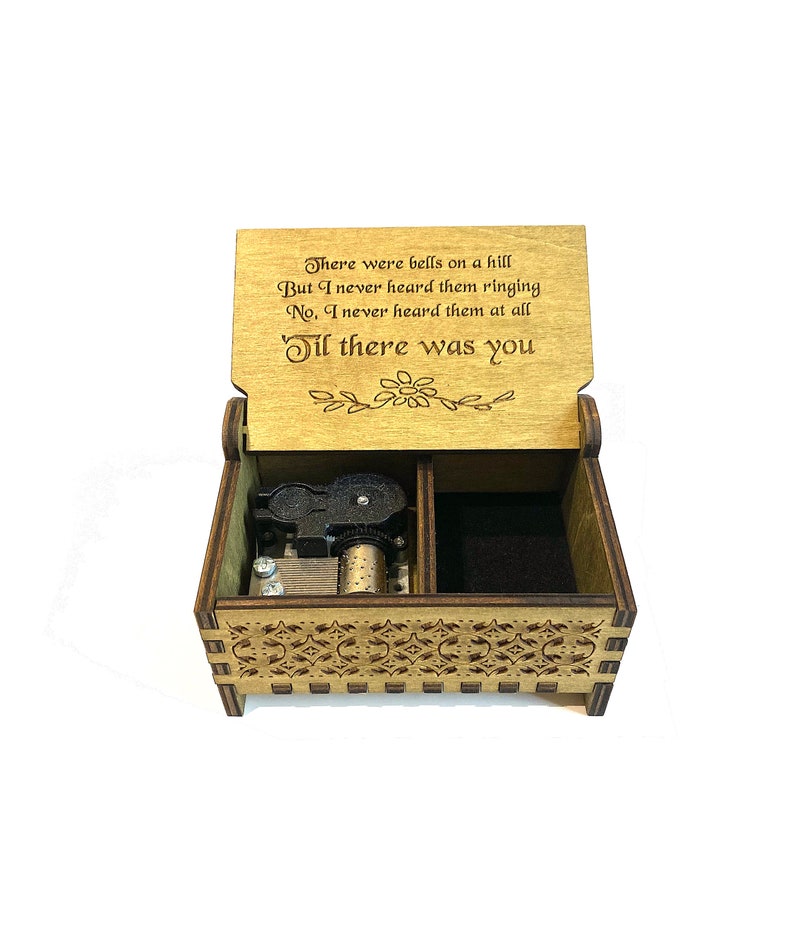 Puede incluir: Caja de m&uacute;sica de madera con un dise&ntilde;o tallado y un mecanismo musical negro. La tapa est&aacute; abierta y presenta una cita: "There were bells on a hill But I never heard them ringing No, I never heard them at all 'Til there was you".