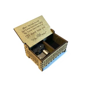 Puede incluir: Una caja de m&uacute;sica de madera con una tapa con bisagras. La tapa est&aacute; abierta y presenta un poema grabado: "There were bells on a hill But I never heard them ringing No, I never heard them at all Til there was you". La caja de m&uacute;sica tiene un mecanismo de cuerda negro y plateado en el interior.