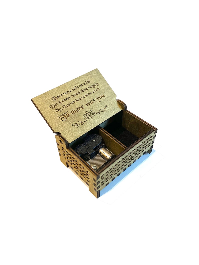 Puede incluir: Una caja de m&uacute;sica de madera con una tapa con bisagras. La tapa est&aacute; abierta y presenta un poema grabado: "There were bells on a hill But I never heard them ringing No, I never heard them at all Til there was you". La caja de m&uacute;sica tiene un mecanismo de cuerda negro y plateado en el interior.