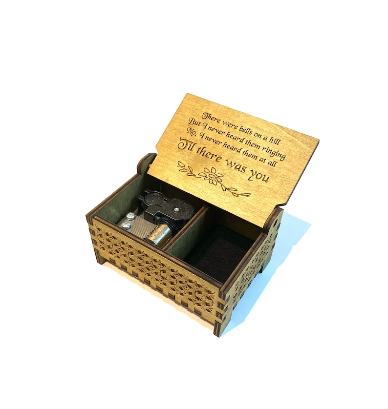 Puede incluir: Caja de m&uacute;sica de madera con tapa abatible. La tapa est&aacute; abierta y presenta una cita grabada con l&aacute;ser: "There were bells on a hill But I never heard them ringing No, I never heard them at all Til there was you".