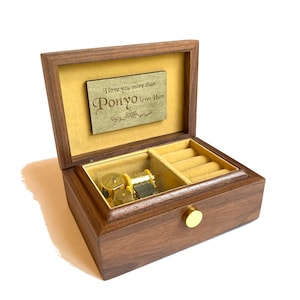 May include: A wooden music box with a glass lid. The box has a small compartment for rings and a music mechanism inside. The lid has a plaque with the inscription "I love you more than Ponyo loves Ham".