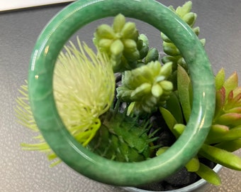 May include: A green jade bangle bracelet, resting on a pot of small green plants.