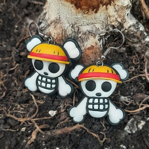 Op de afbeelding: Een paar witte schedel oorbellen met gele en rode hoeden. De oorbellen zijn gemaakt van polymer clay en hebben zilveren haakjes.