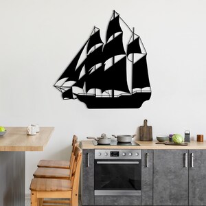 May include: Black metal silhouette of a sailing ship mounted on a white wall above a kitchen counter with wooden cabinets and a stainless steel oven.