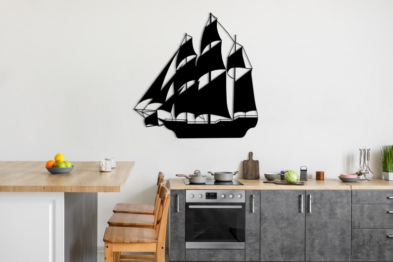 May include: Black metal silhouette of a sailing ship mounted on a white wall above a kitchen counter with wooden cabinets and a stainless steel oven.