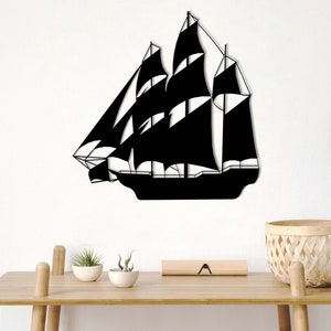 May include: Black metal silhouette of a sailboat with multiple sails, mounted on a white wall. The sailboat is centered in the image and is the main focus.