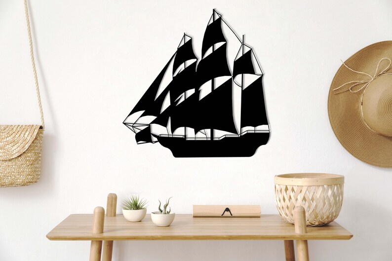 May include: Black metal silhouette of a sailboat with multiple sails, mounted on a white wall. The sailboat is centered in the image and is the main focus.
