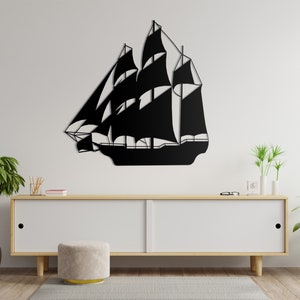 May include: Black metal silhouette of a sailboat with multiple sails, mounted on a white wall above a white dresser with a light wood top. The dresser is in a room with wood floors and two potted plants.