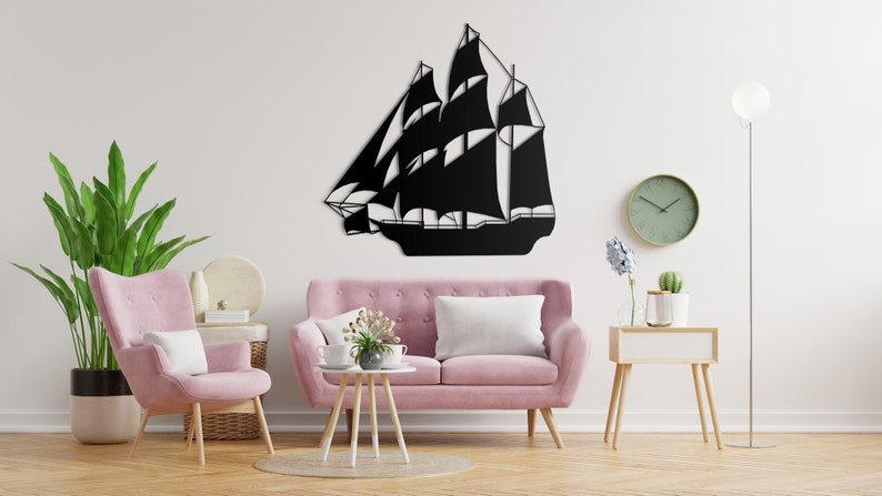 May include: Black metal wall art depicting a sailboat with a white background. The art is displayed on a white wall above a pink sofa in a living room setting.