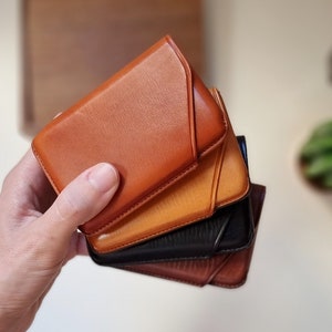 leather card cases are shown in one hand in the four different colors available. You can personalize them with your initials or name to make it unique. Pictured is the card case in havana, brown, black and honey.