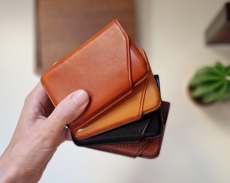leather card cases are shown in one hand in the four different colors available. You can personalize them with your initials or name to make it unique. Pictured is the card case in havana, brown, black and honey.
