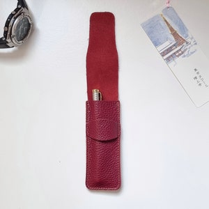 Burgundy leather pencil pouch. The pen case is shown open, with a ballpoint pencil inside, you can see that it can hold two pens. This pen holder closes with a flap.