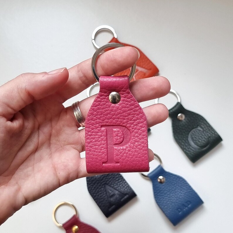 on one hand is a small fuchsia pink full-grain soft leather key ring engraved with the uppercase letter P.