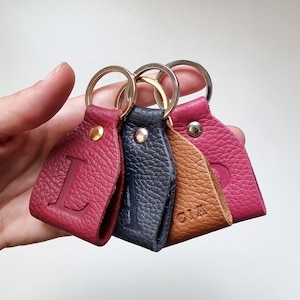 Four small handmade full grain leather key rings with engraved initials. The first is the initial L in burgundy, the second is the initial A in navy blue, the third with the name Lucia engraved in brown, and the fourth in fuchsia with the letter P.