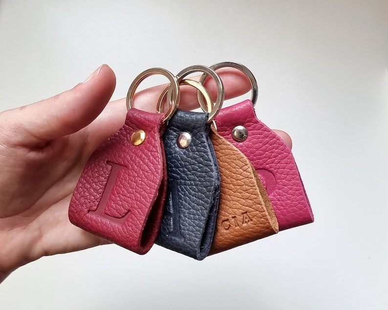 Four small handmade full grain leather key rings with engraved initials. The first is the initial L in burgundy, the second is the initial A in navy blue, the third with the name Lucia engraved in brown, and the fourth in fuchsia with the letter P.