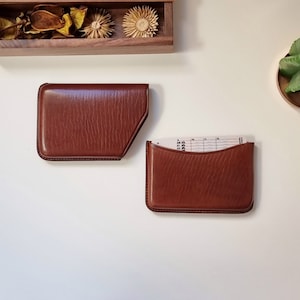 brown colored leather card holder shown on a table and open. This card holder opens by pulling the case to one side.
