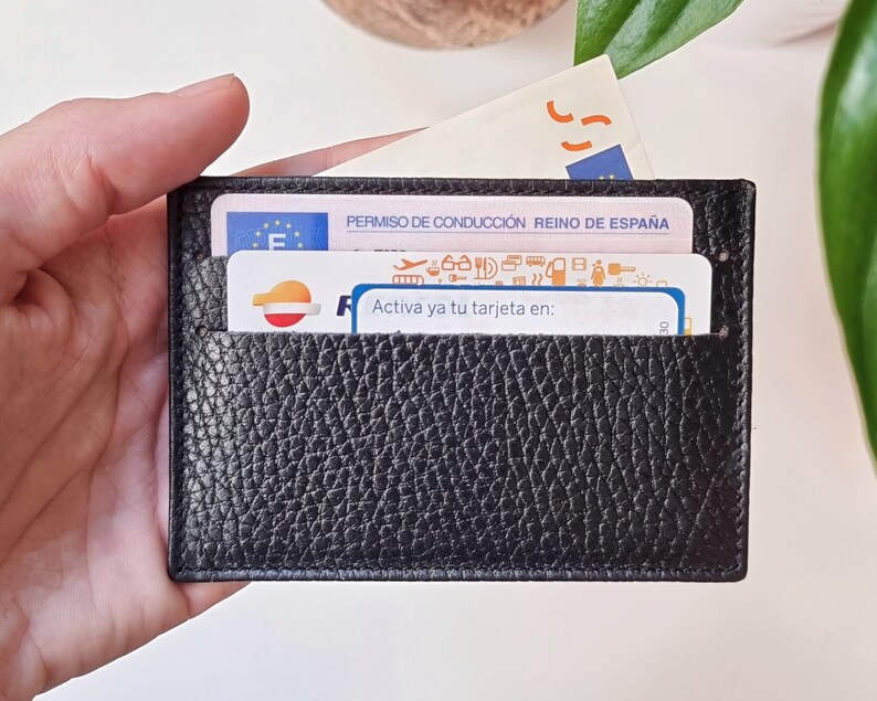 Slim leather card holder in black color, with two card slots on each side and a central compartment. In the two front slots you can see two cards and in the central compartment a bill that comes out
