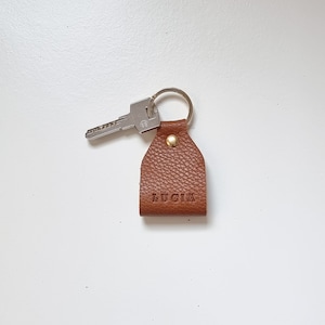 Small leather keychain engraved with five initials (name of Lucia). Brown color, full grain leather.