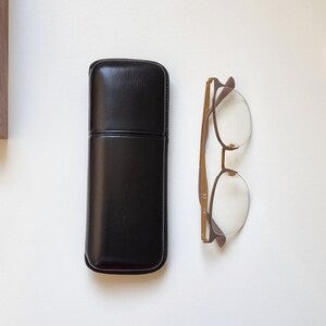 May include: A black leather glasses case with a brown metal frame glasses with clear lenses.