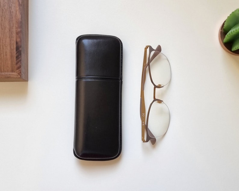 May include: A black leather glasses case with a brown metal frame glasses with clear lenses.
