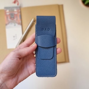 Leather pen case, it closes with a flap and the DAD monogram is engraved on the top. This pen holder is blue. It is shown close up to appreciate the high quality full grain leather with which it is handmade.