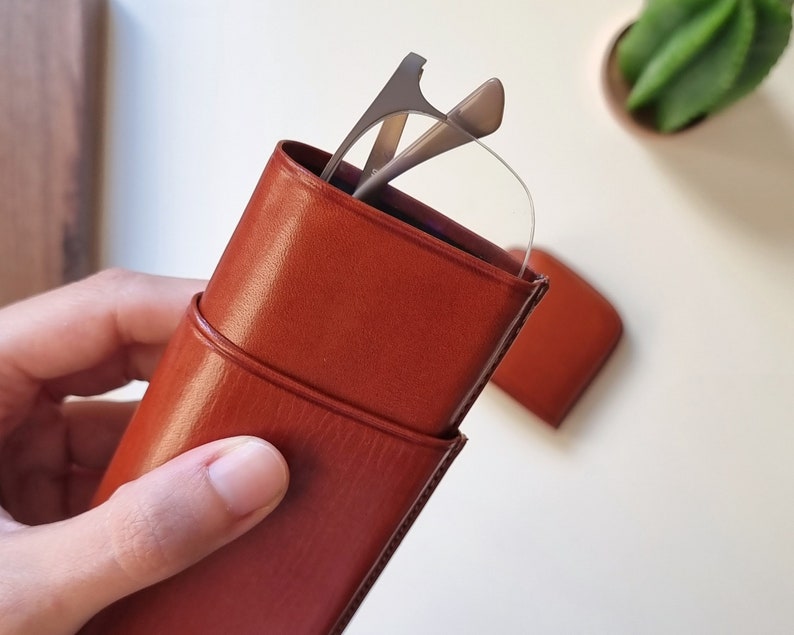May include: A brown leather glasses case with a pair of silver reading glasses inside.