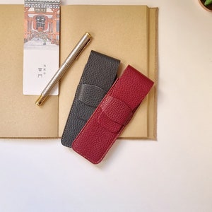 two leather pen holders, one in burgundy and the other in gray. each holds two pens. They close with a flap. The leather with which they are handmade is of high quality and very soft.